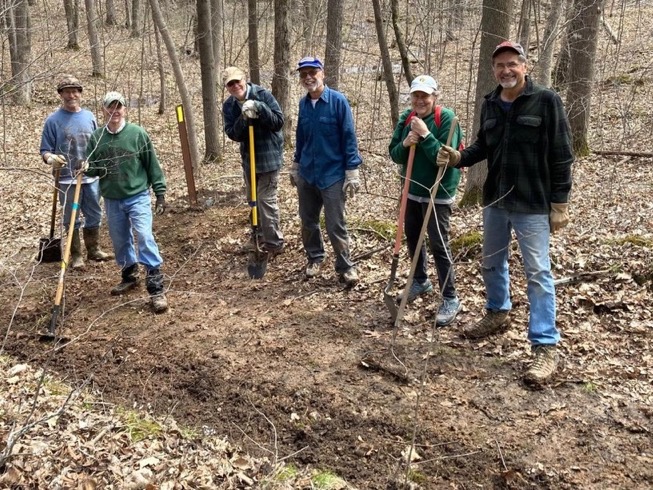 A group of trail volunteers caught in the act, pose with tools